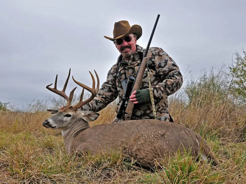 A hunter kneels in the woods behind a deer.