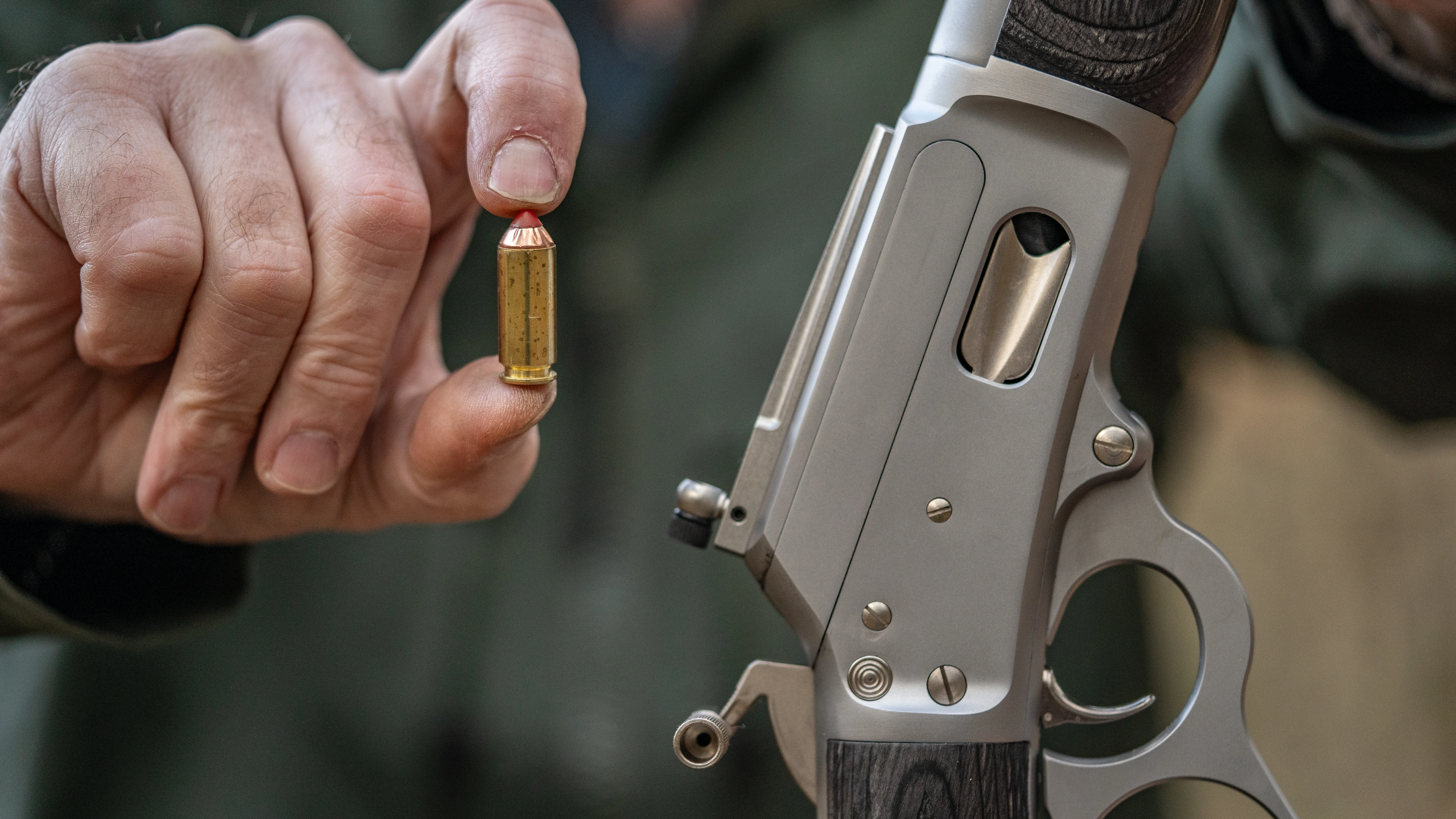 A man holds up a 10mm Auto cartridge in one hand and Marlin's 1894 Trapper in the other.