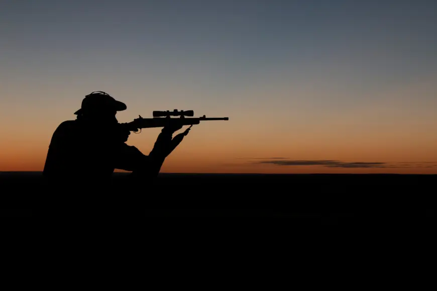 Silhouette of a man aiming a rifle against the sunset.