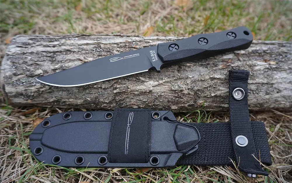 The black Ka-Bar EK Commando knife on a bark log on a lawn.