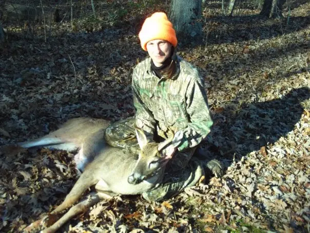 A woman hunter sits next to a whitetail deer she killed