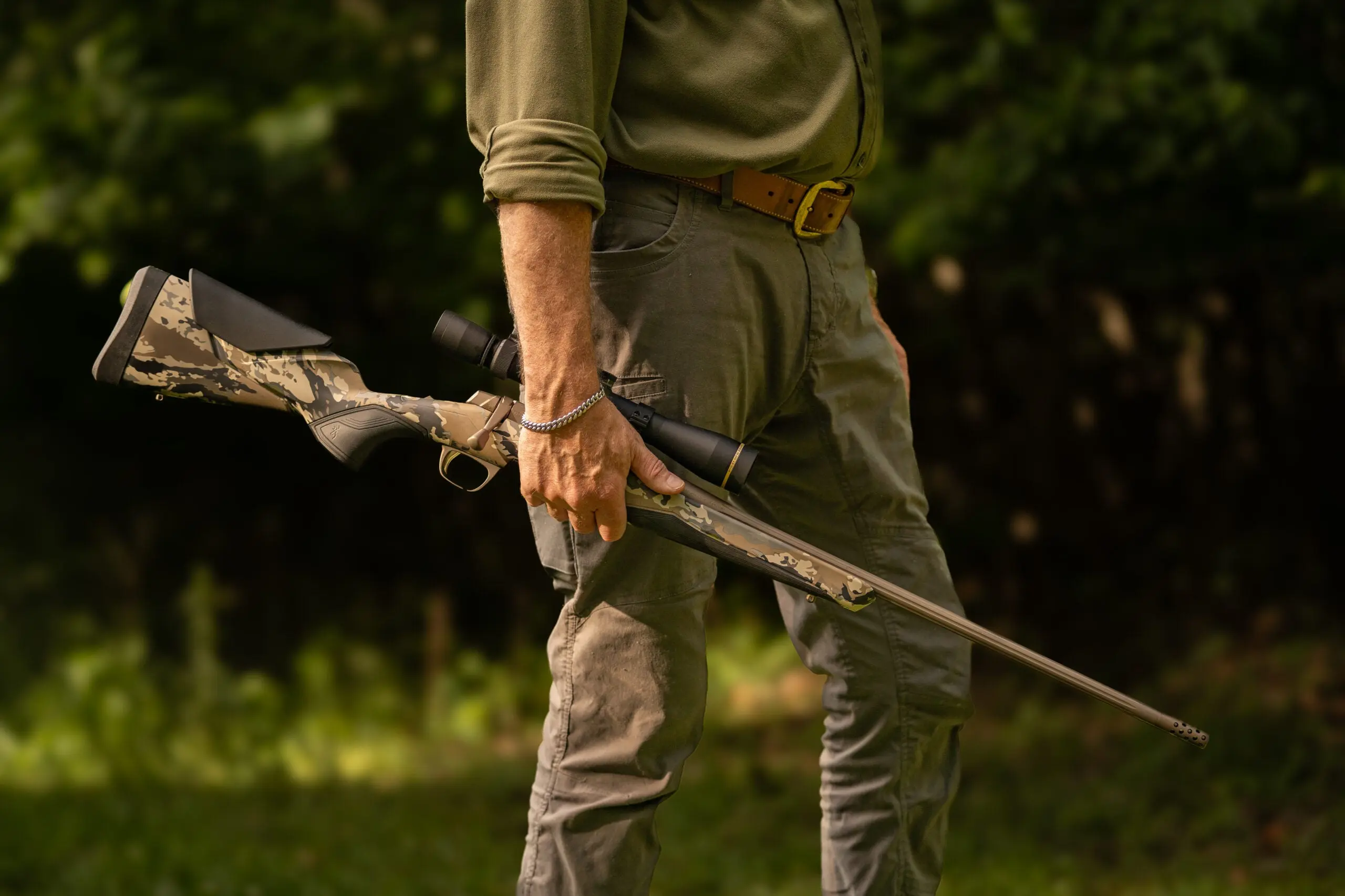 A shooter walks onto a summer outdoor range, carrying the Browning X Bolt 2 Speed MB rifle in his right hand.