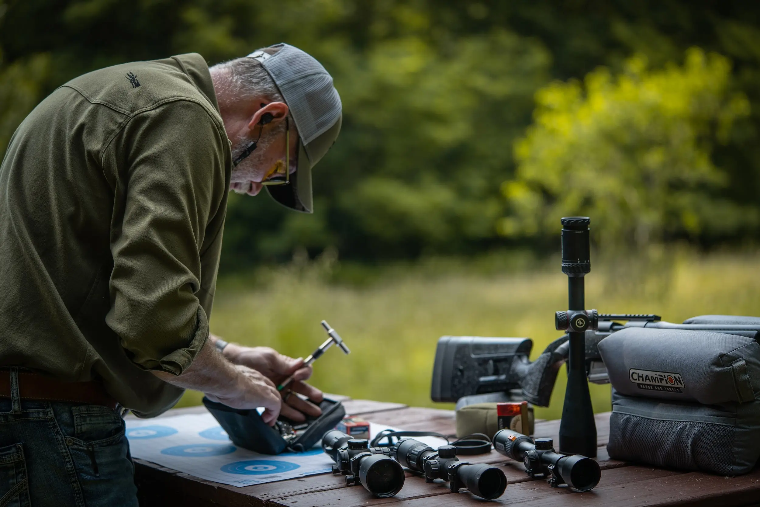 Man measuring a rifle scope on a bench.