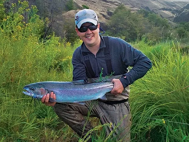 An angler holds up a large steelhead fish.