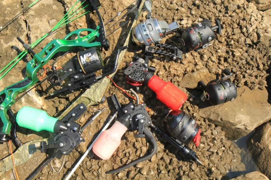 Eight bowfishing reels on lay on rocks next to a compound bow