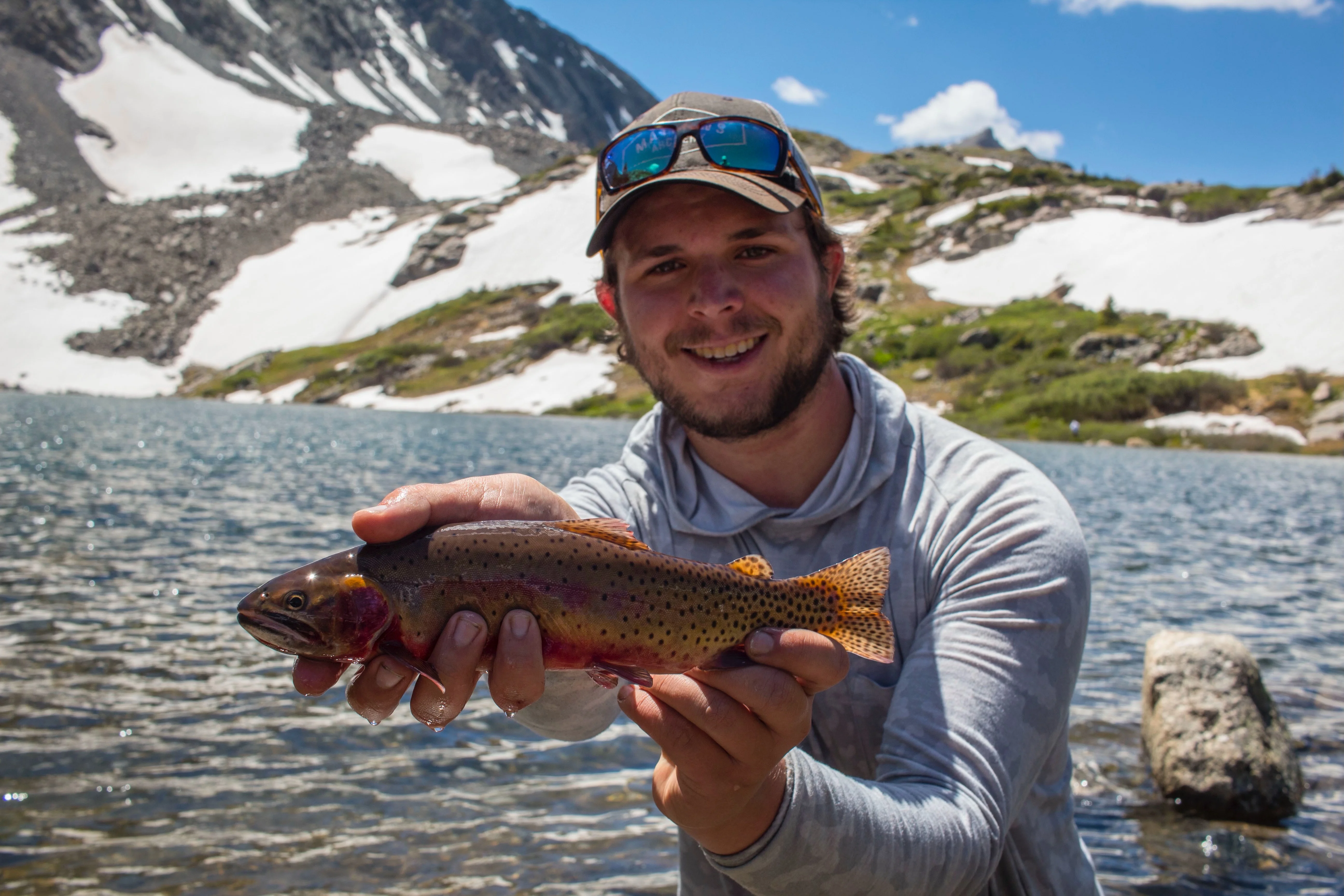 Angler holds up cutthroat trout next to alpine lake