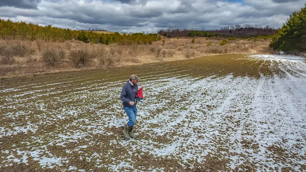 Photo of man spreading seed on a field, showing when to plant food plots for deer.
