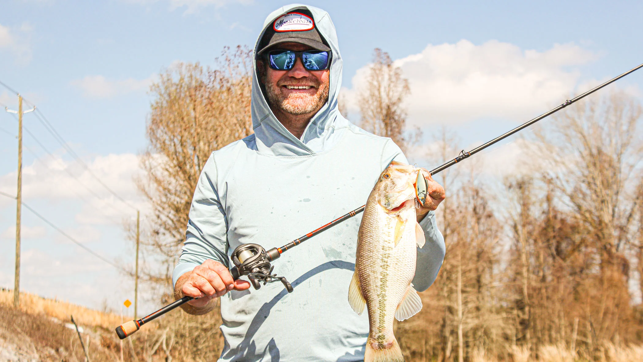 Bass angler holds up largemouth bass with fishing rod in other hand