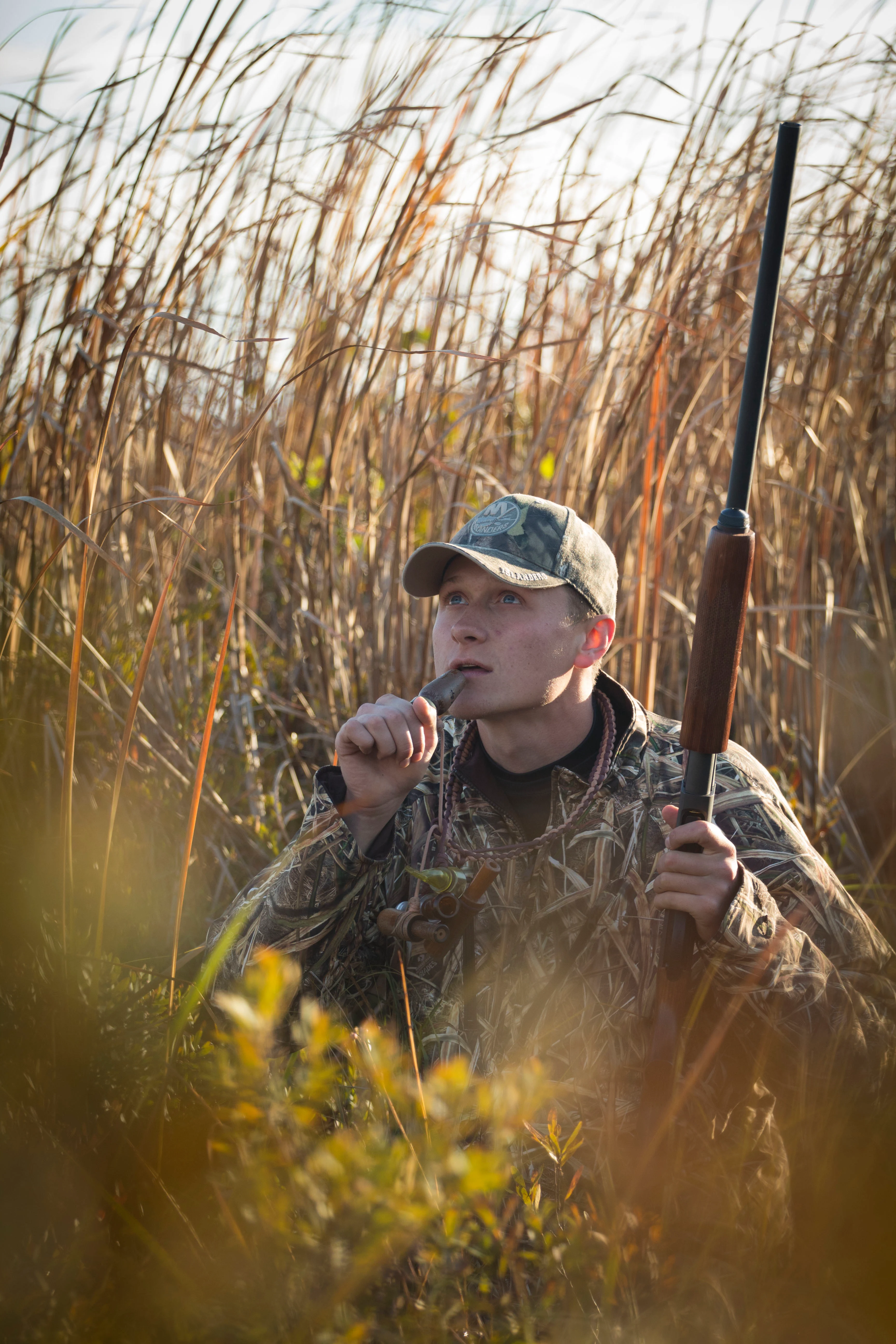 Duck hunter holds a call to his mouth as he looks toward the sky