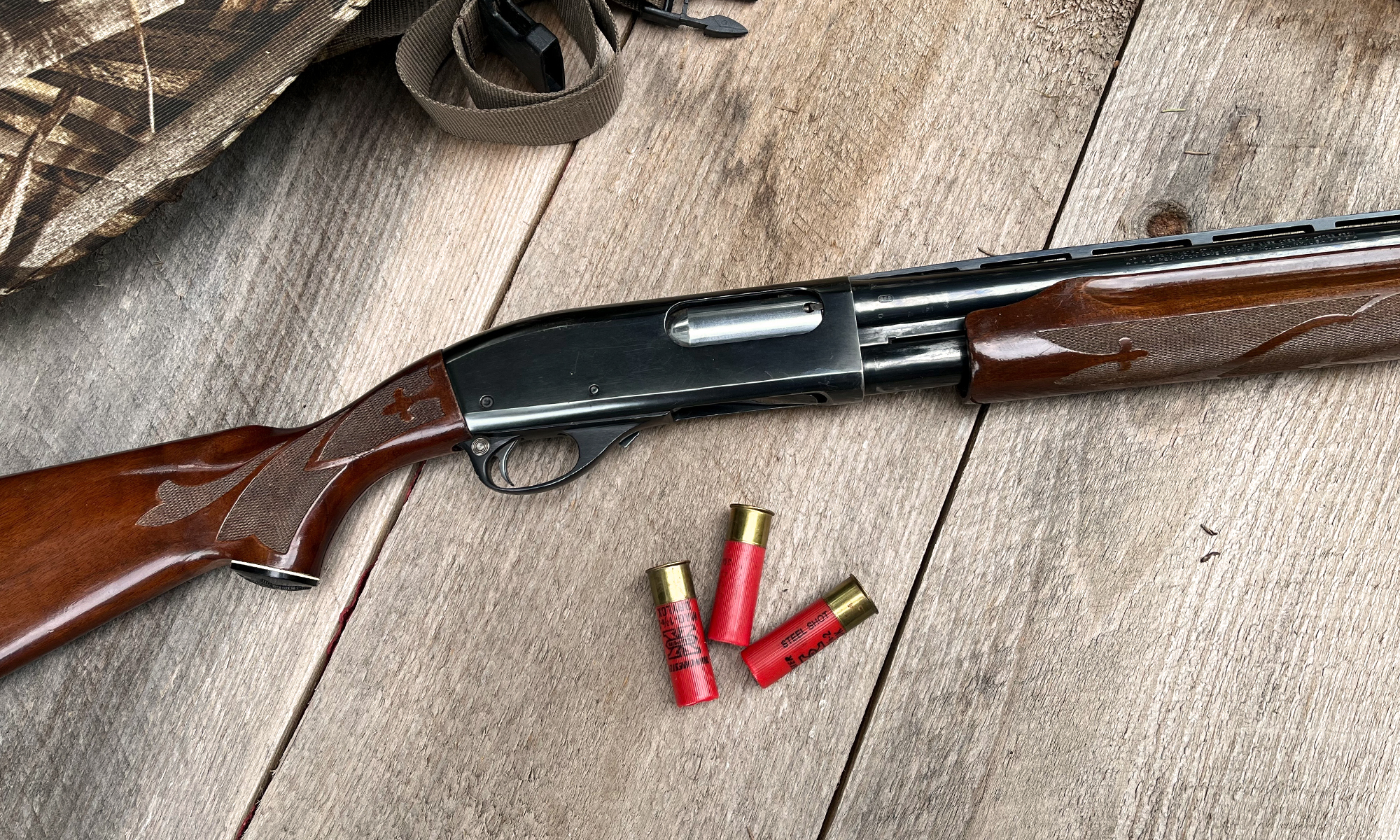 A Remington 870 on barn boards with three shotgun shells. 