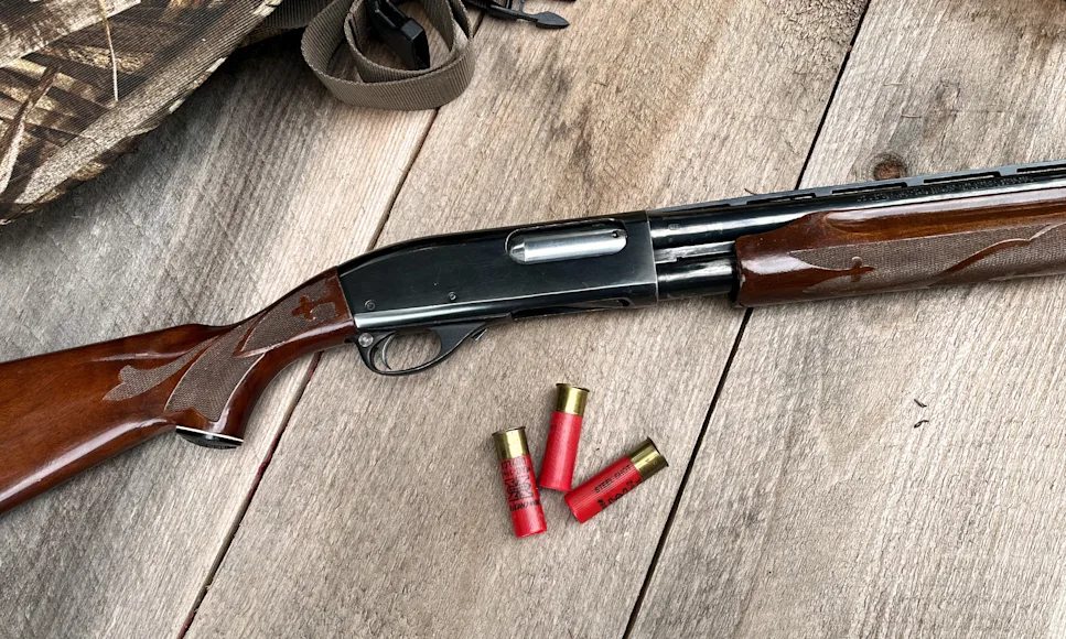 A Remington 870 on barn boards with three shotgun shells.