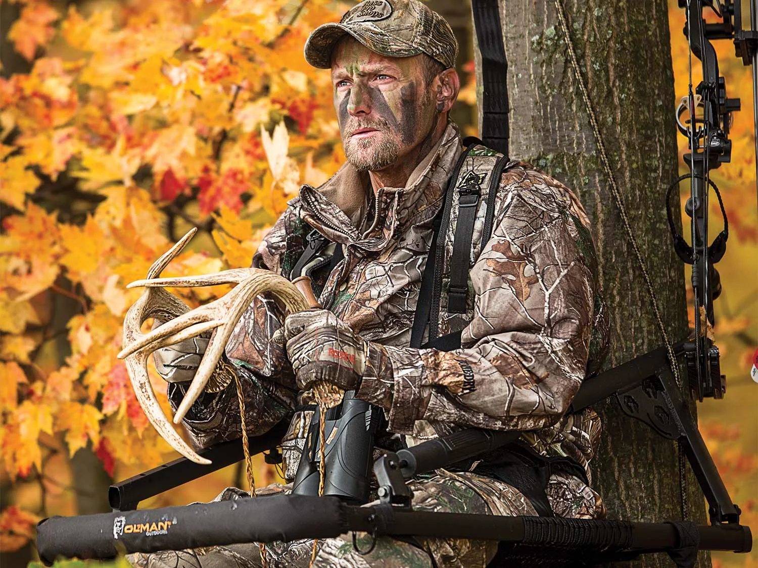 A deer hunter in a tree stand hits rattling antlers together. 