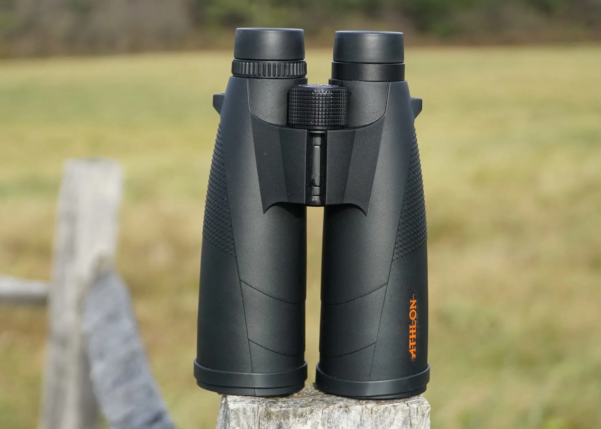 Athlon Cronus 15x56 binocular sitting on a fence post with field in background.