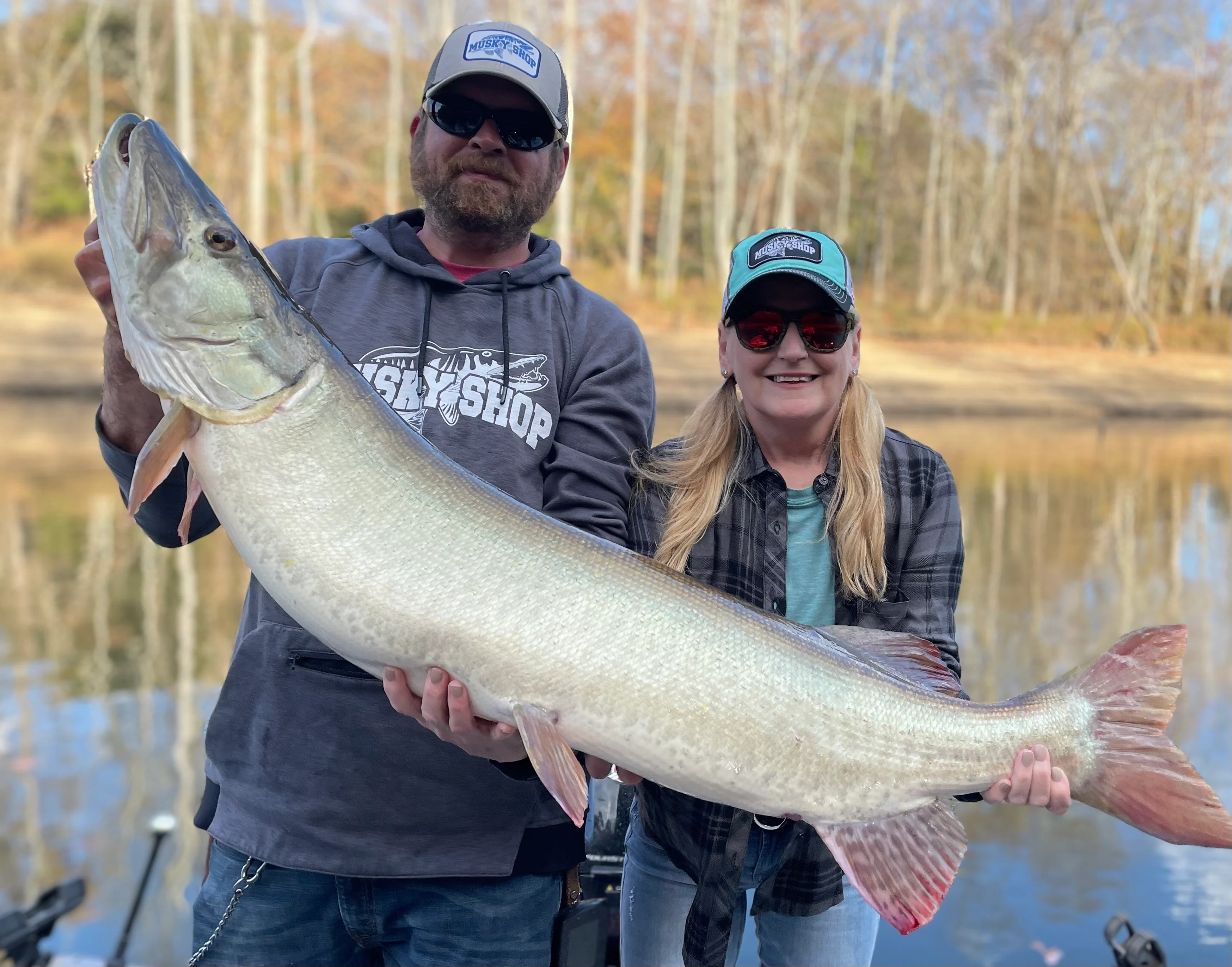 A man and a woman in a boat holding up a huge muskie