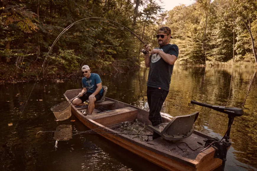 Two fisherman in Field & Stream t-shirts fish from a small boat on a pond.