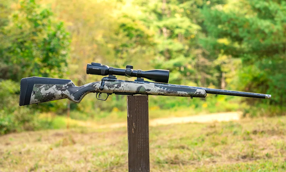 The new Savage 110 Ultralite Camo bolt-action rifle balanced on a post in a field.
