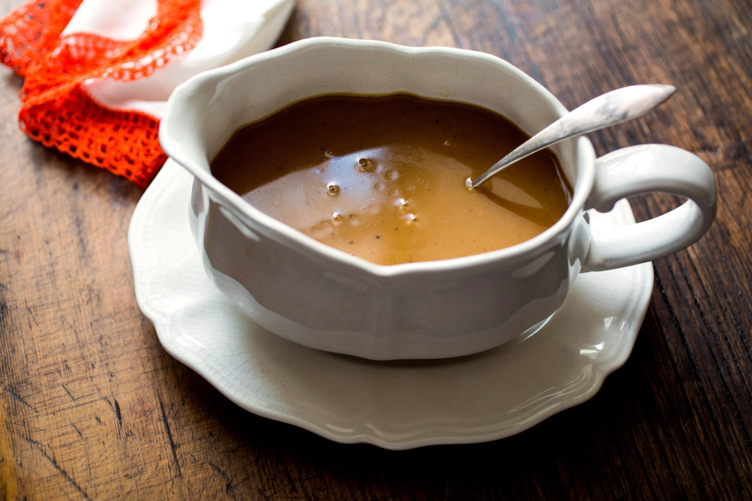 Turkey giblet gravy served in a white gravy bowl and saucer on a wooden table