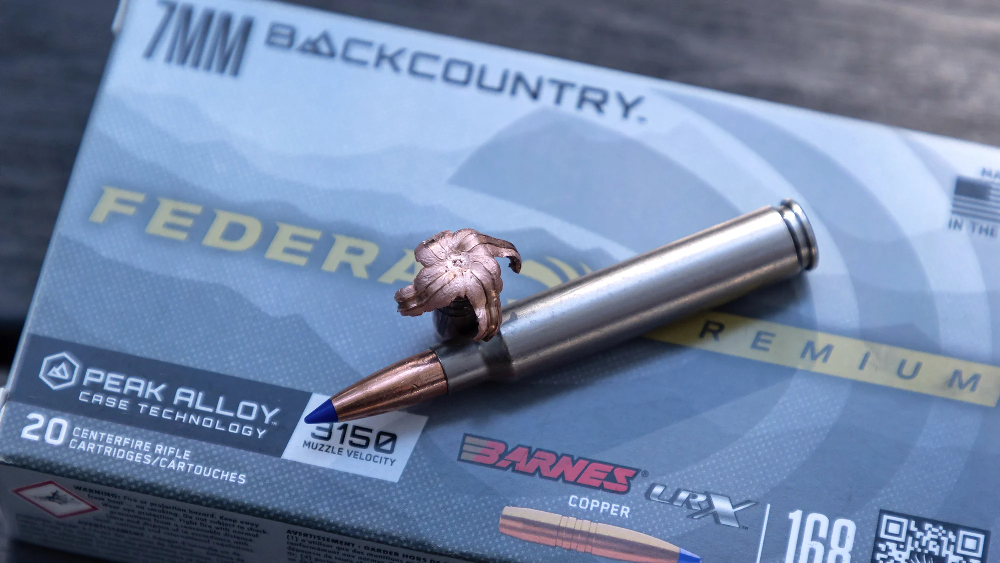 A single cartridge and a fired bullet rest on a box of new Federal 7mm Backcountry ammo.