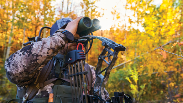 Bowhunter looking through Leupold binoculars in woods