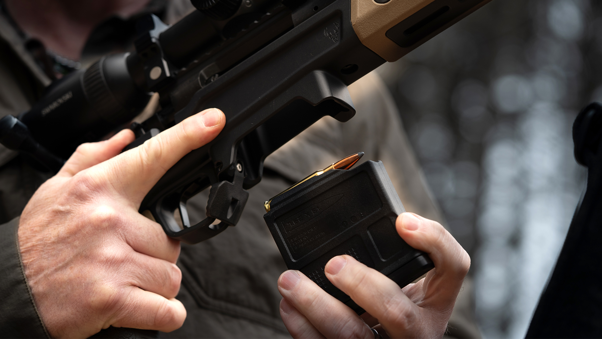 A shooter loads a magazine into a rifle