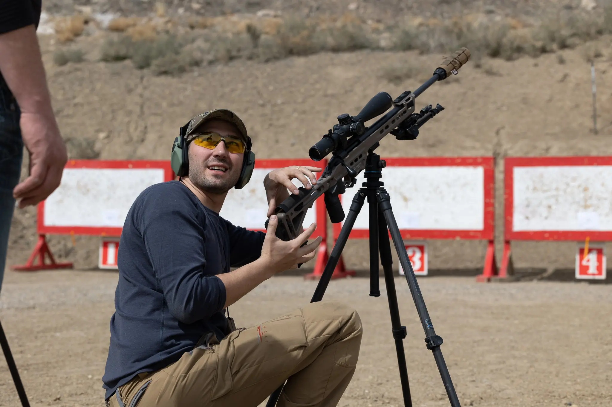 A man next to a rifle on a tripod having a conversation.