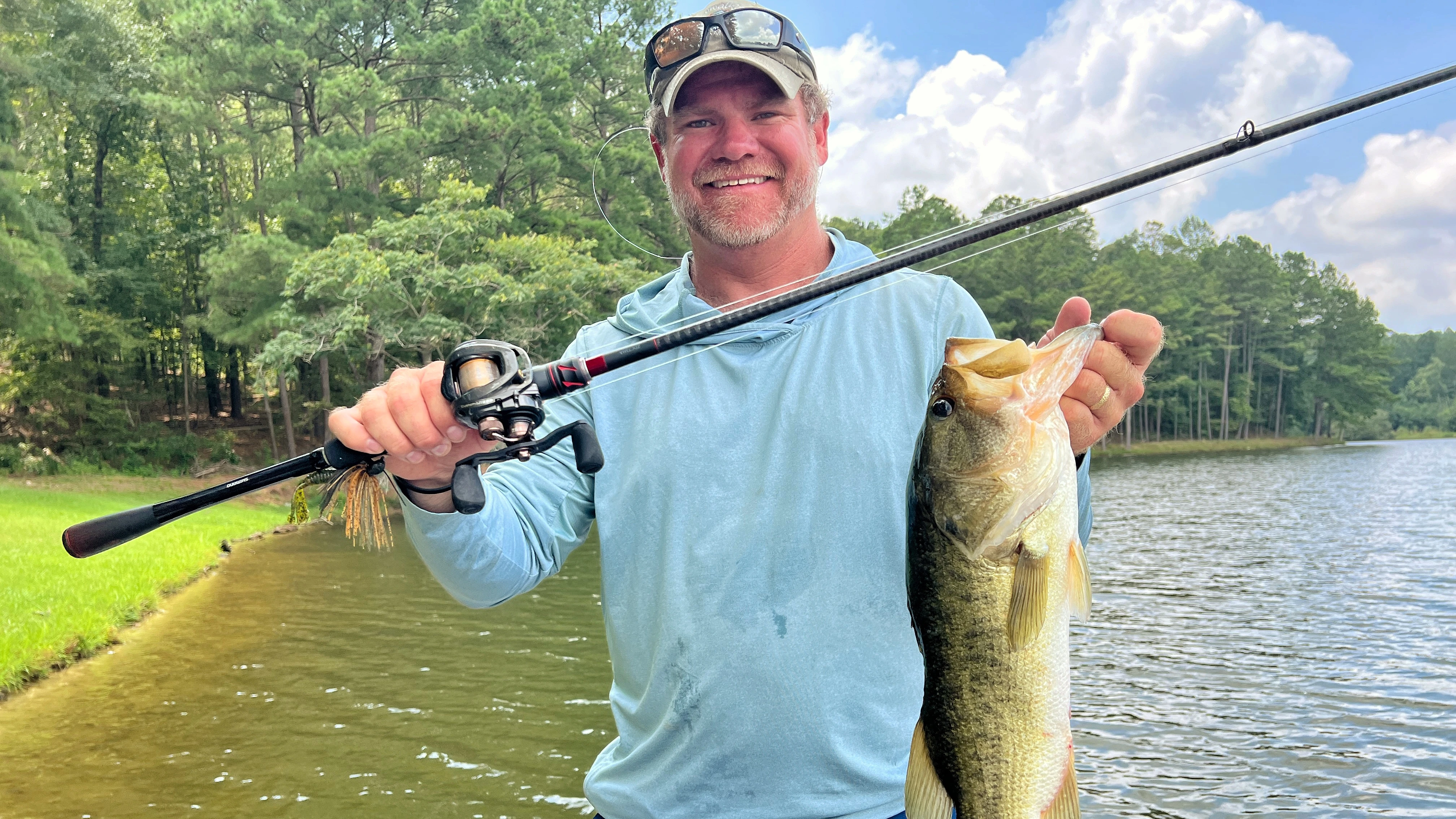 Angler holds up bass in one hand and fishing rod in the other hand