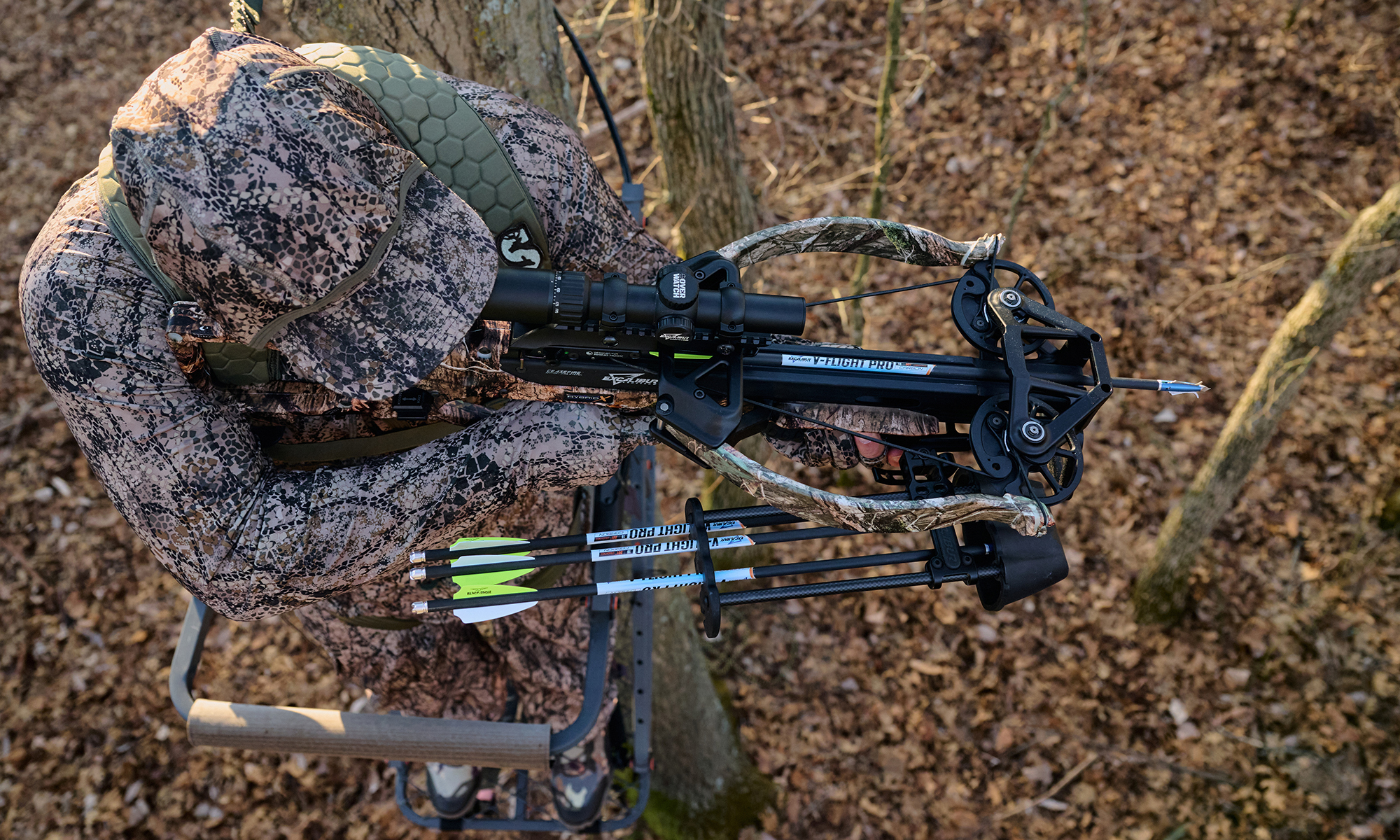 A hunter shoots a crossbow from a tree stand in the woods. 
