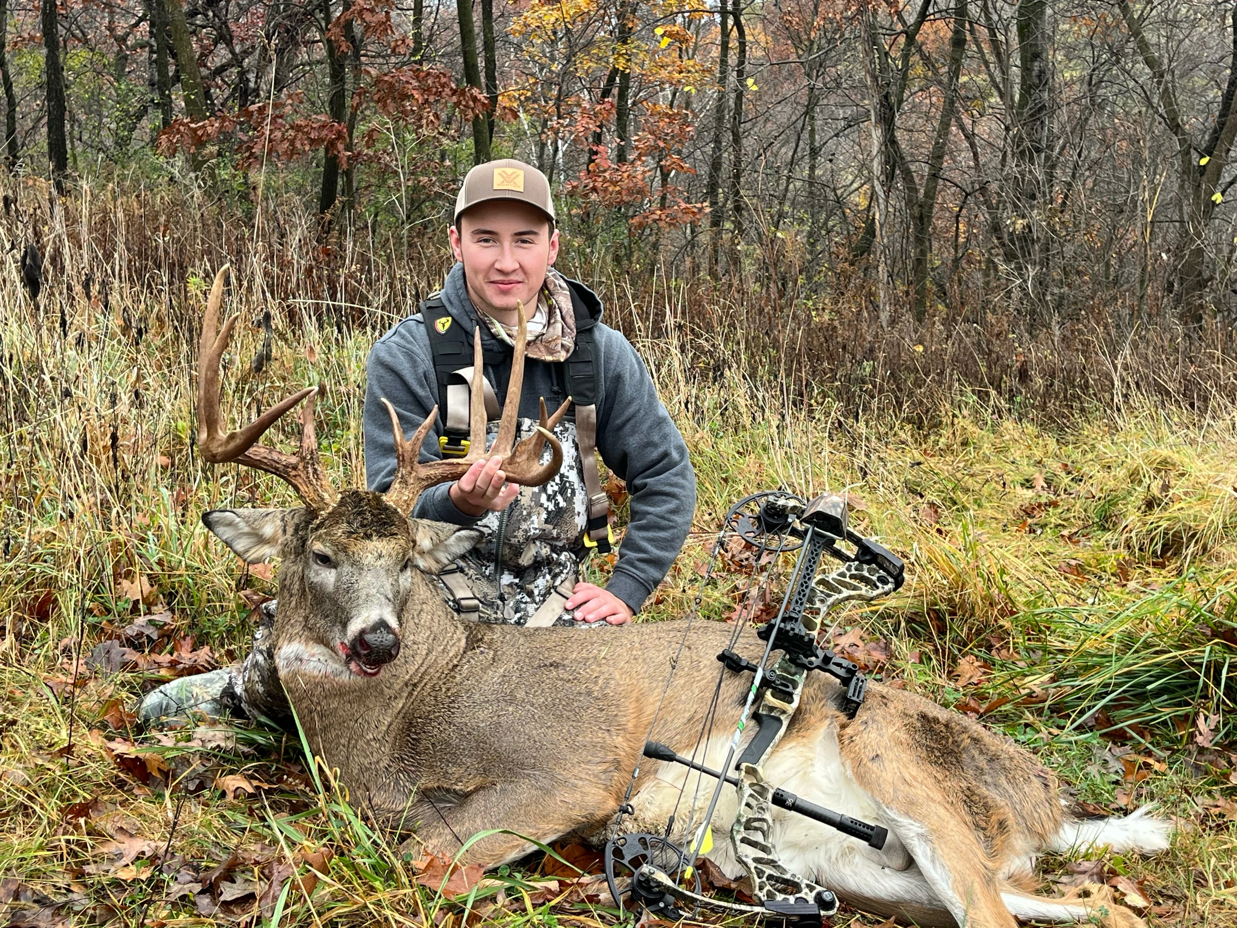 A young hunter sits o the ground showing off a trophy whitetail buck he took with a bow. 