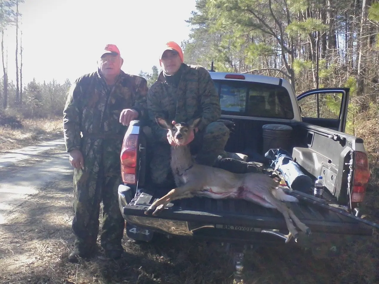 Two hunters pose with a dead whitetail deer from a pickup truck