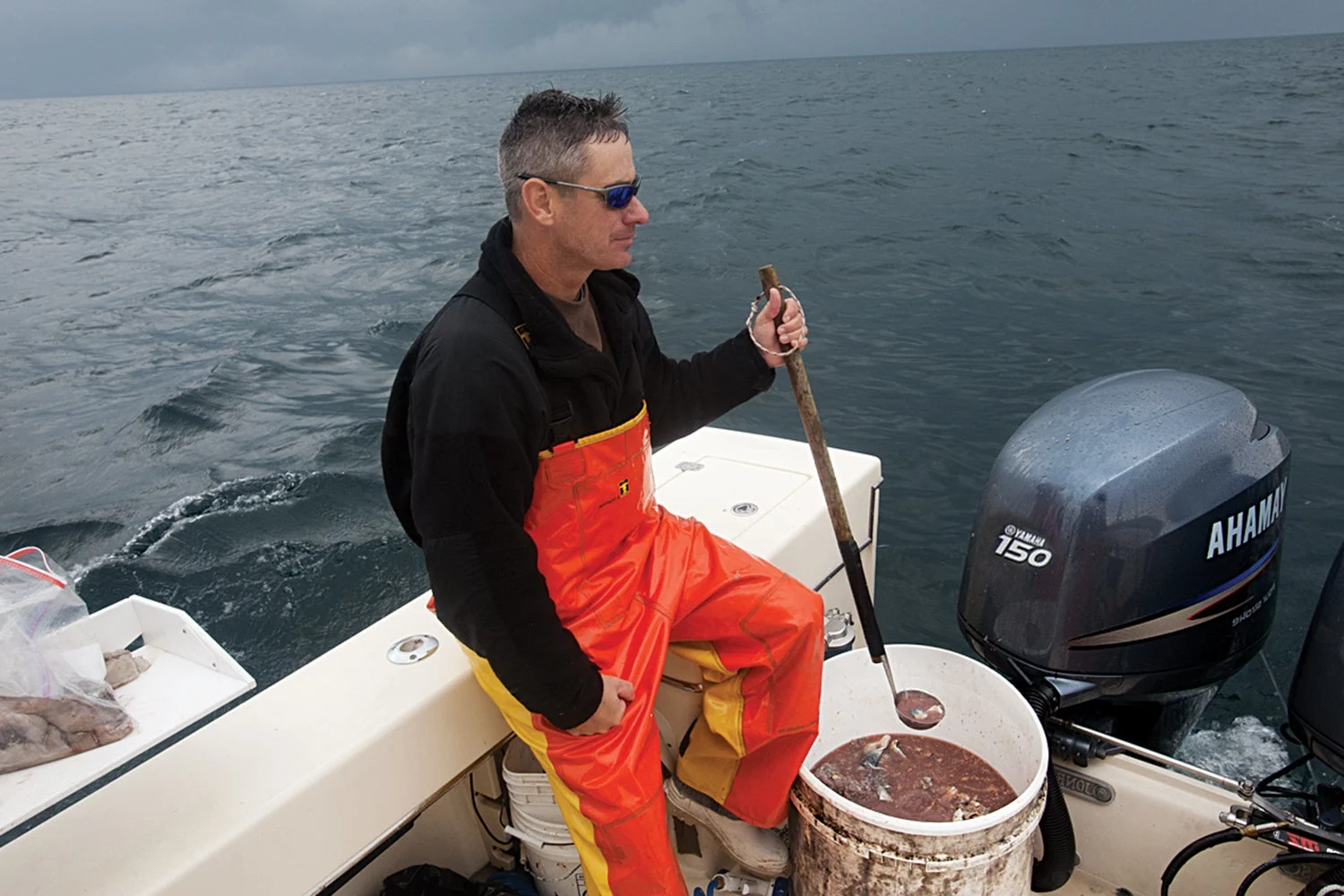 Man seated at back of boat holds ladle of cut-up fish