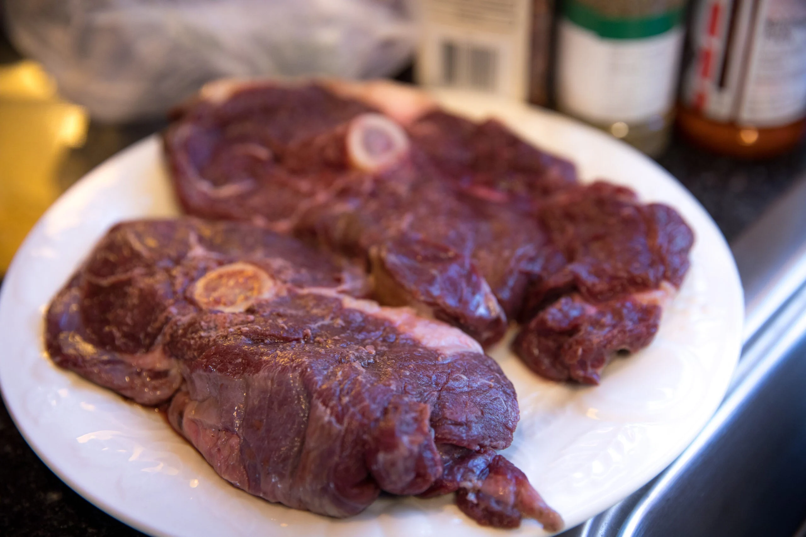 Raw bear steaks on a white plate sitting on a kitchen counter