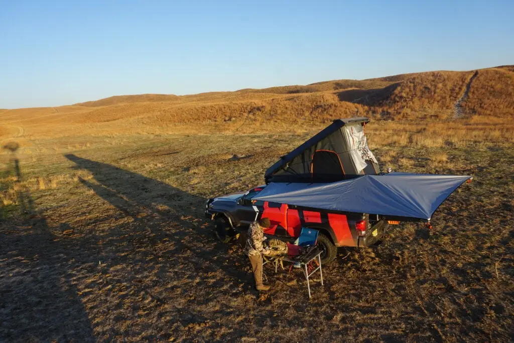 Toyota Tacoma overlanding rig with a rooftop camper and awning in a field.