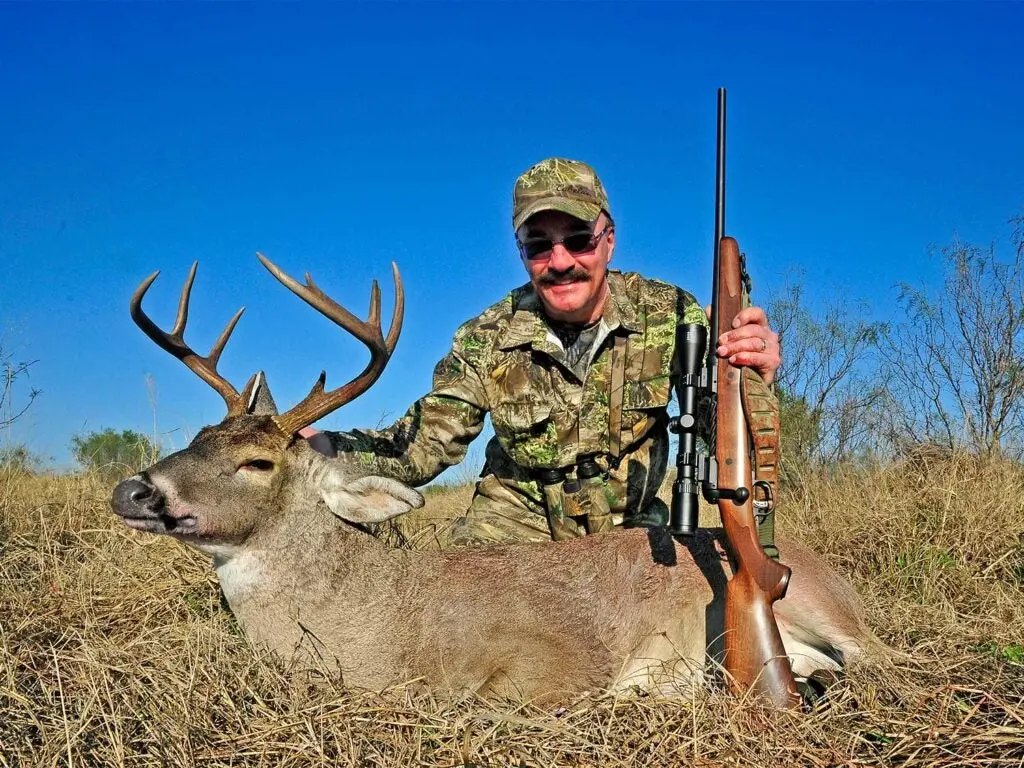 hunter kneeling behind a duck while holding a savage rifle