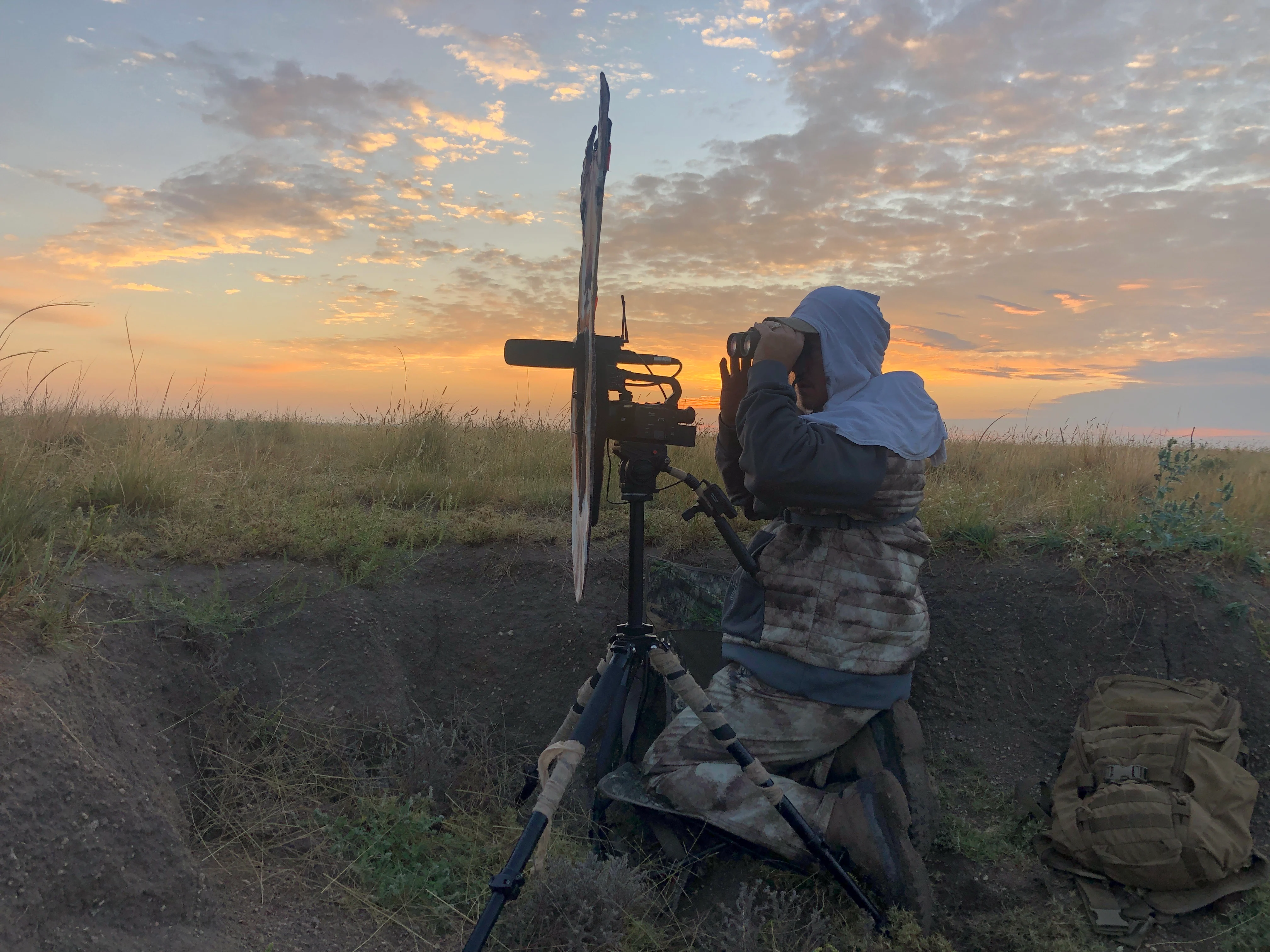 Hunter sits behind a pronghorn decoy with the sun setting in the distance