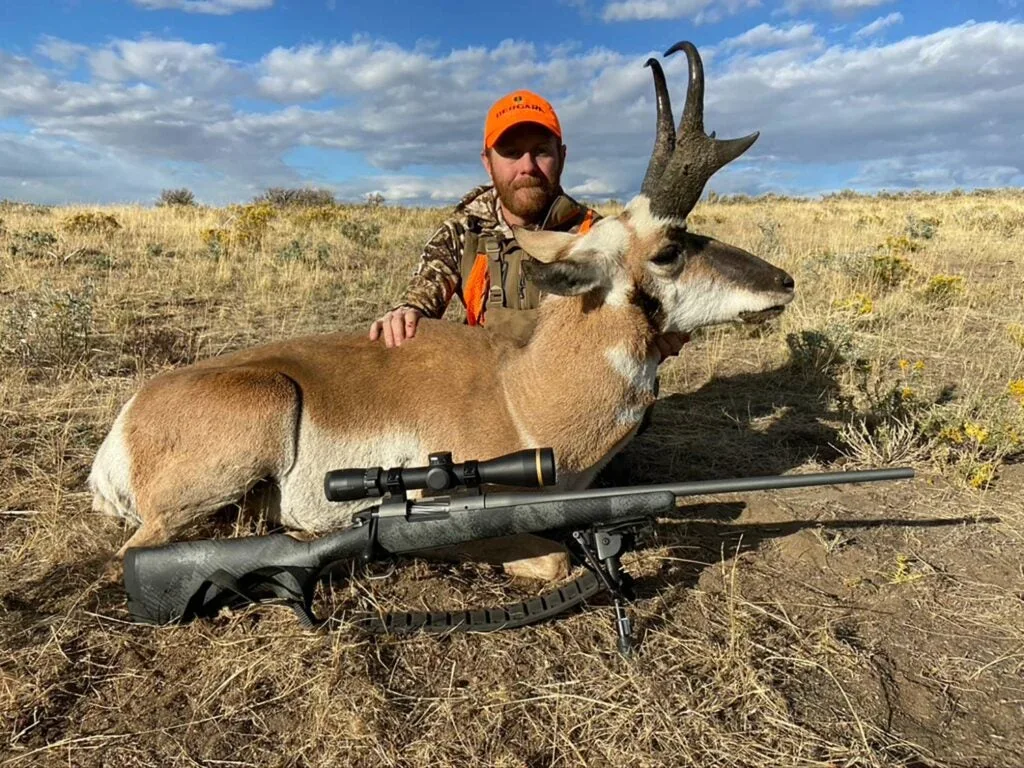 A hunter kneels behind a large antelope in an open field.