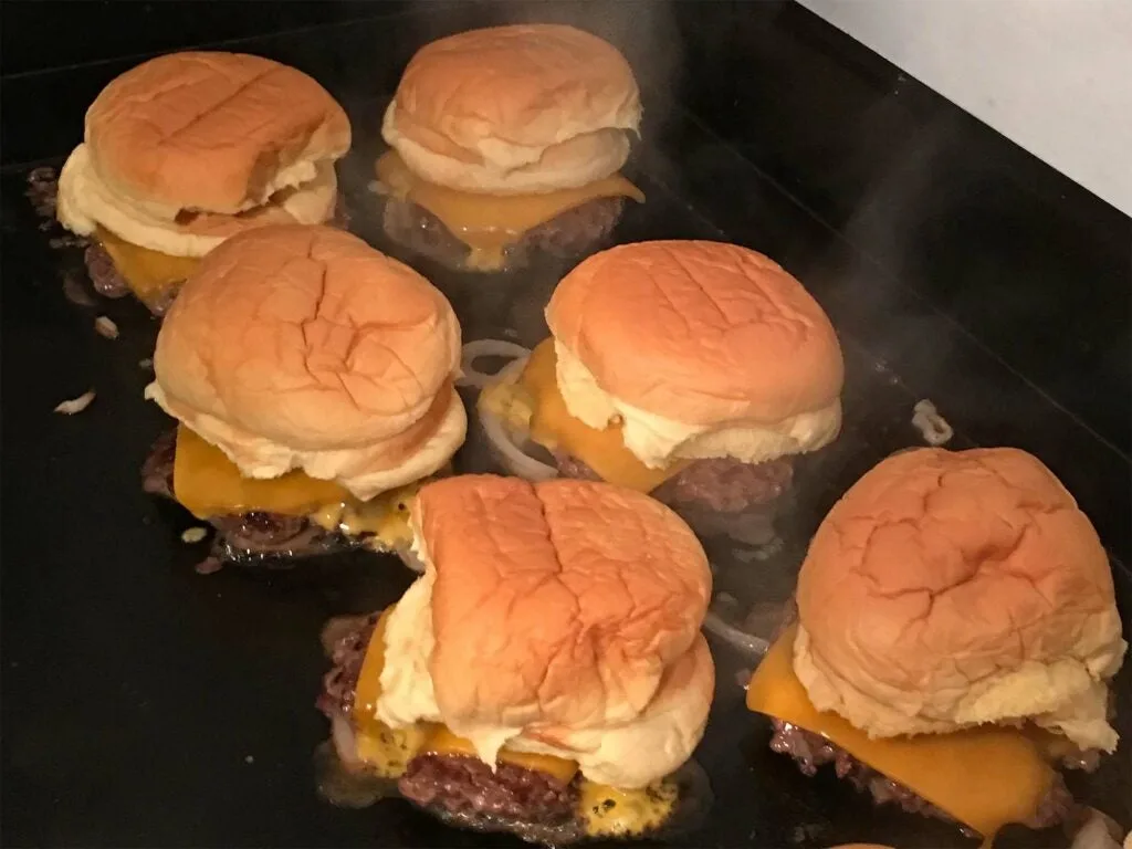 Six venison burgers are cooking on a griddle.