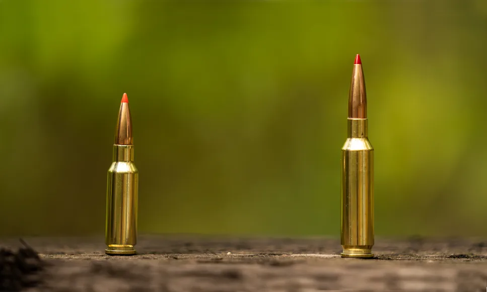6.5 Grendel (left) and 6.5 Creedmoor cartridges standing up on a wooden plank.
