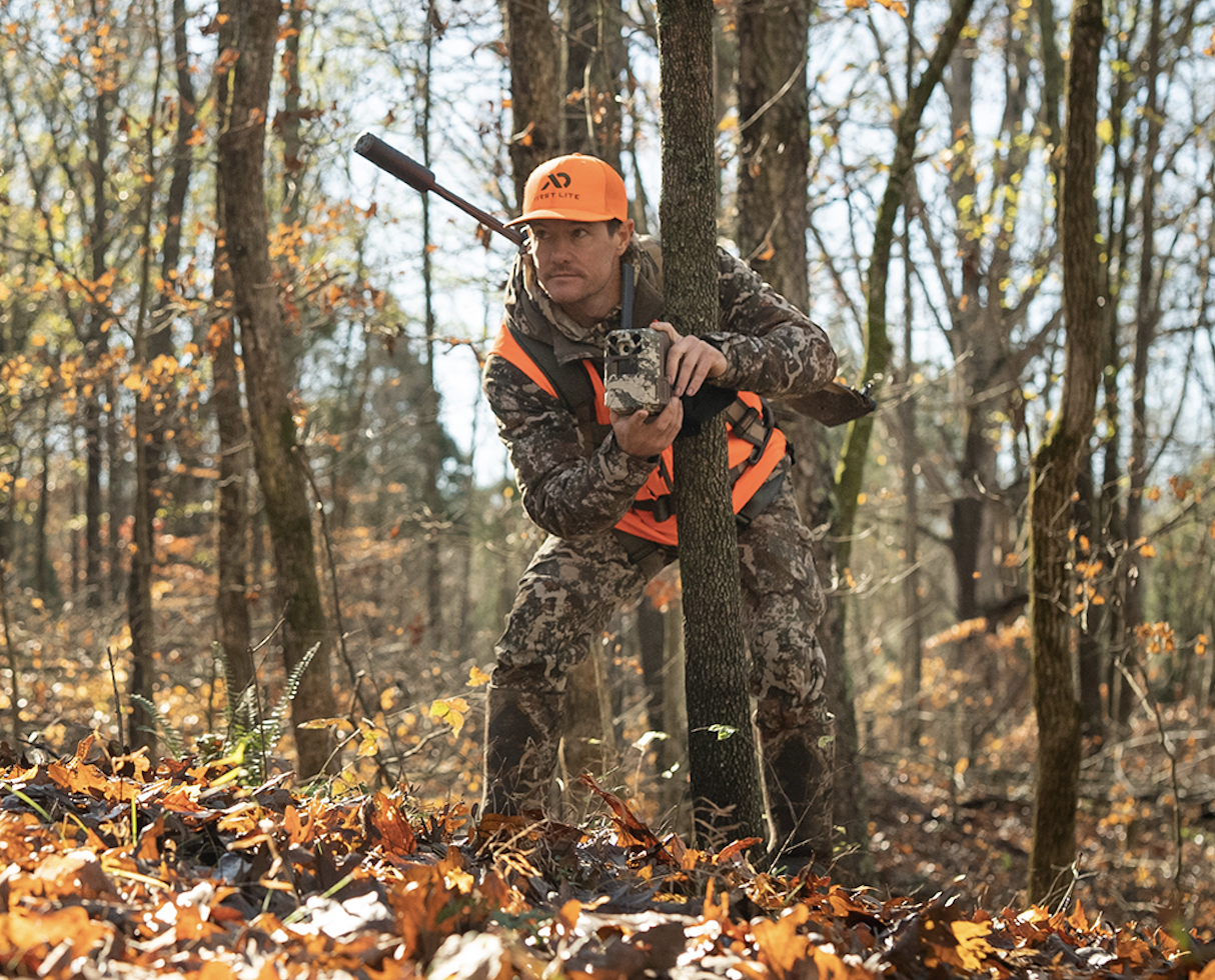 A hunter sets up a trail camera in the woods.