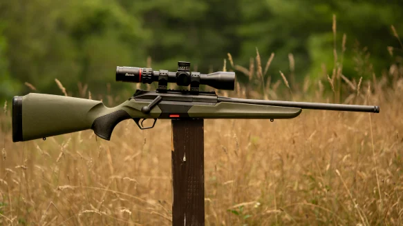 Beretta BRX1 bolt-action rifle sitting on a post in a field with woods in background.