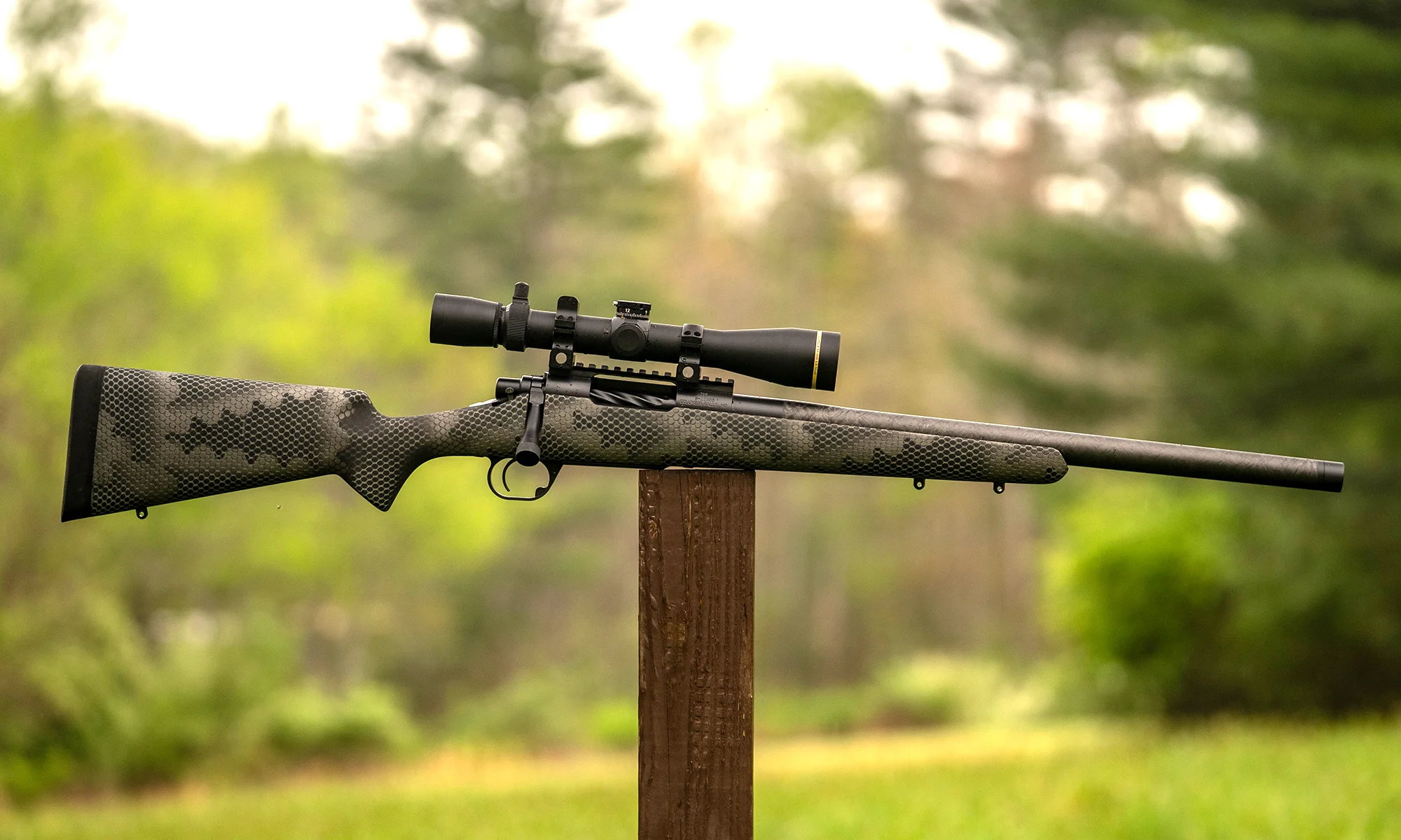 The new Proof Research Glacier Ti bolt-action rifle balanced on a post with woods in the background.