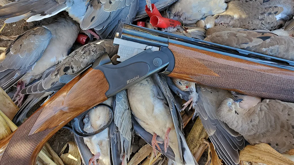 A Rizzini BR110 over-under shotgun resting in a dove field with harvested birds.