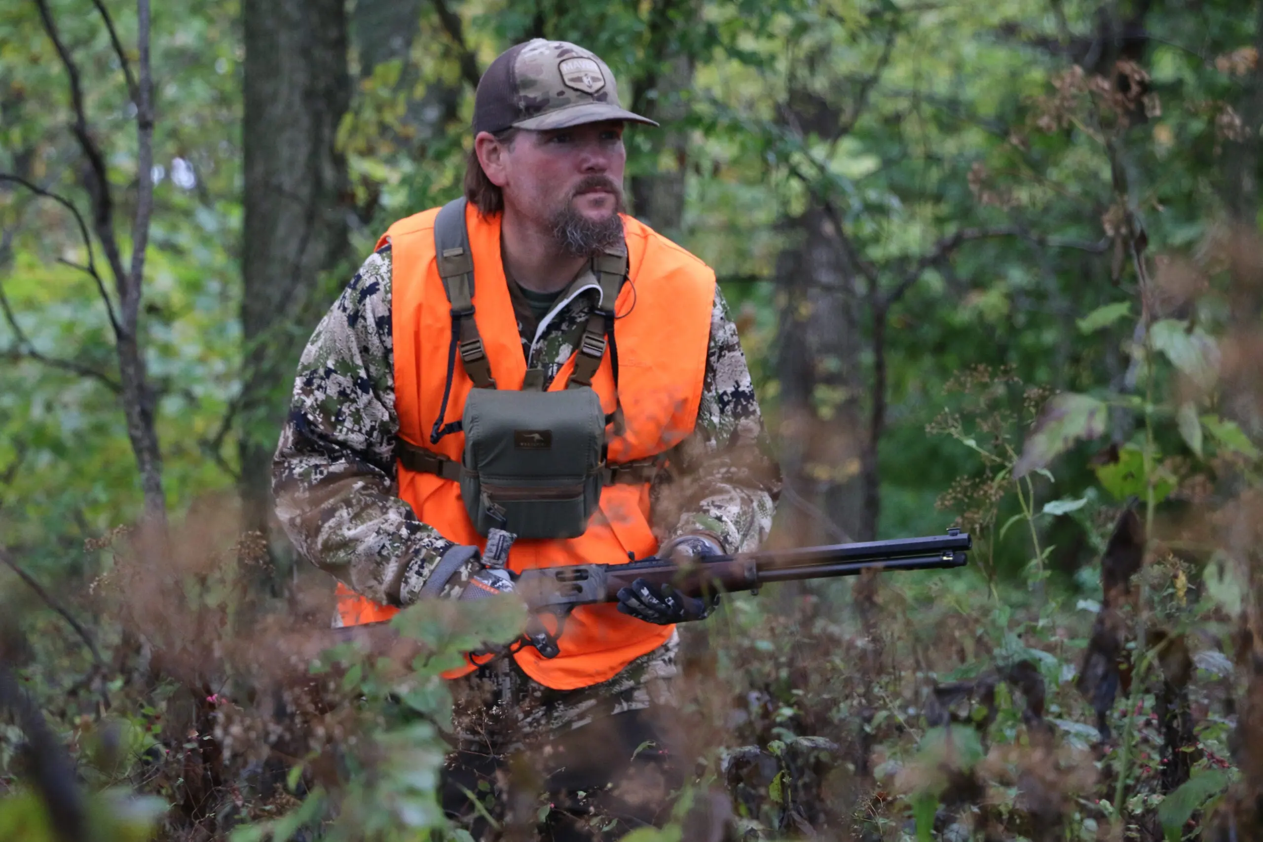 Hunter walking through the woods with a rifle.