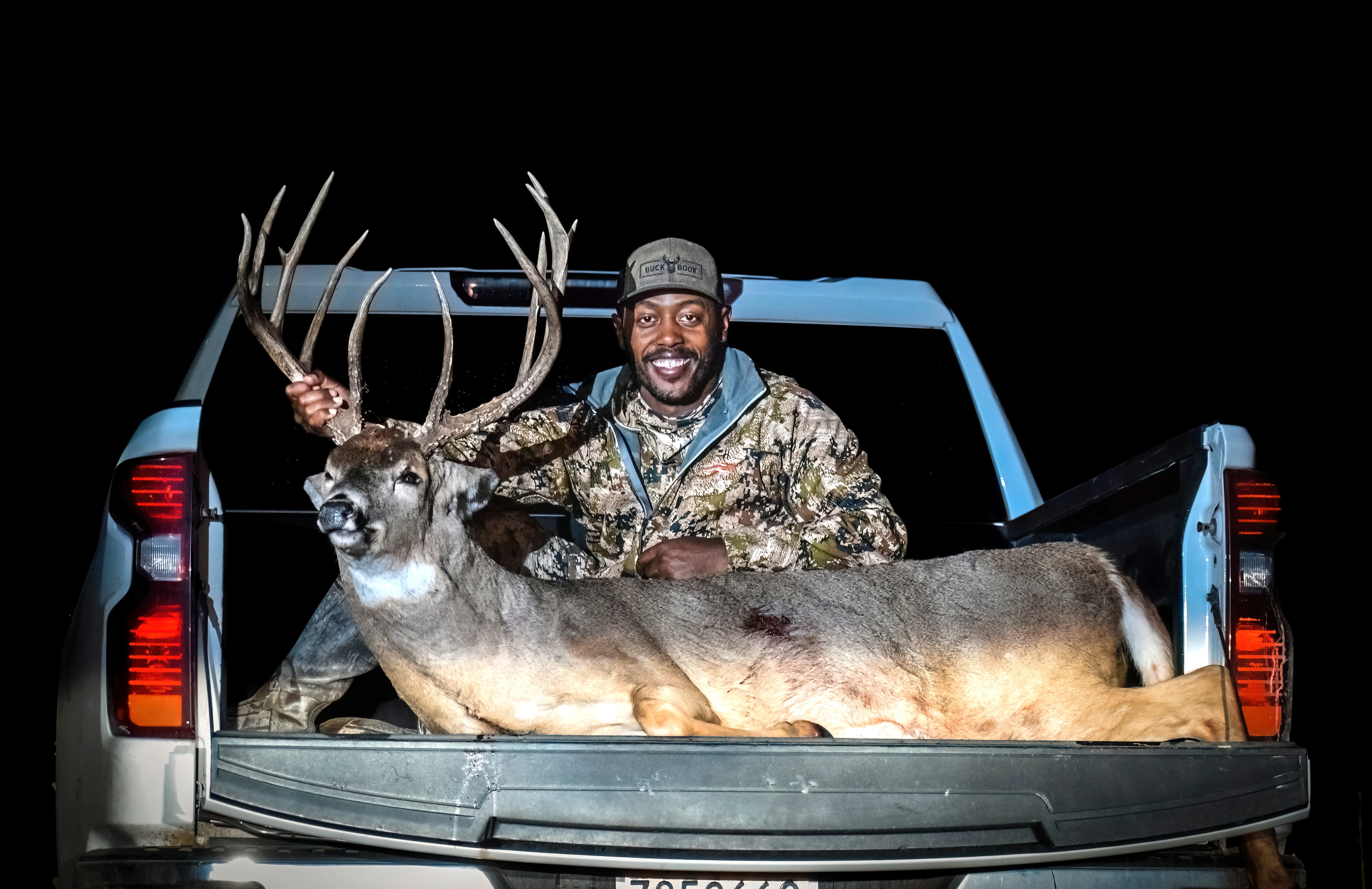 Kansas hunter poses with a giant whitetail buck in the bed of a pickup truck. 