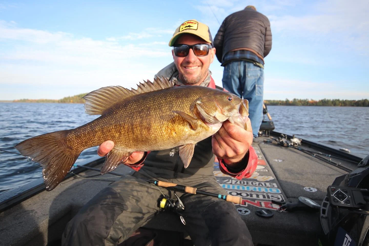 Bassmaster Classic champion Jeff Gustafson holds up a big smallmouth bass in a boat on a lake.