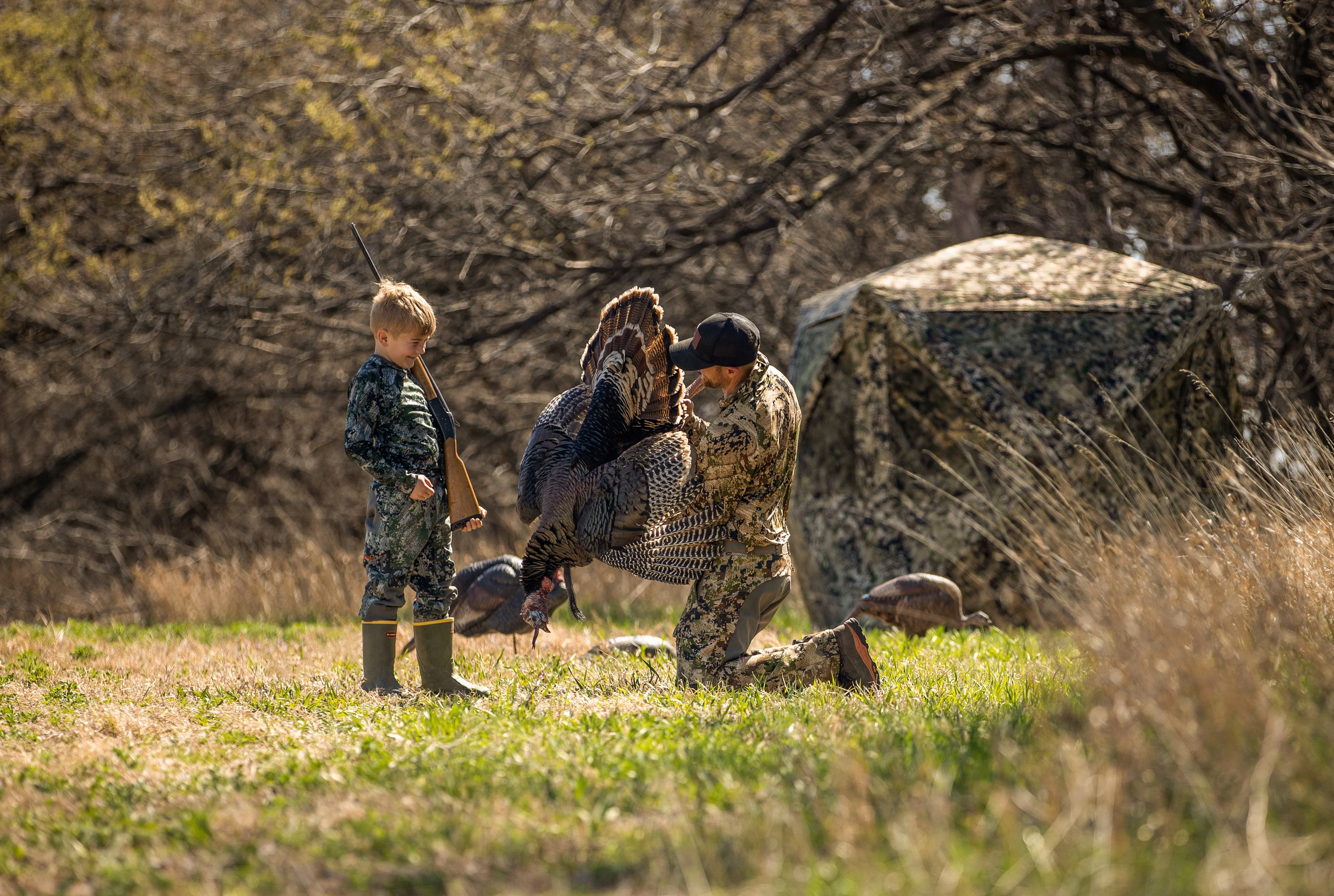 A man shows off a tom turkey taken by a boy from a ground blind on the edge of a field. 