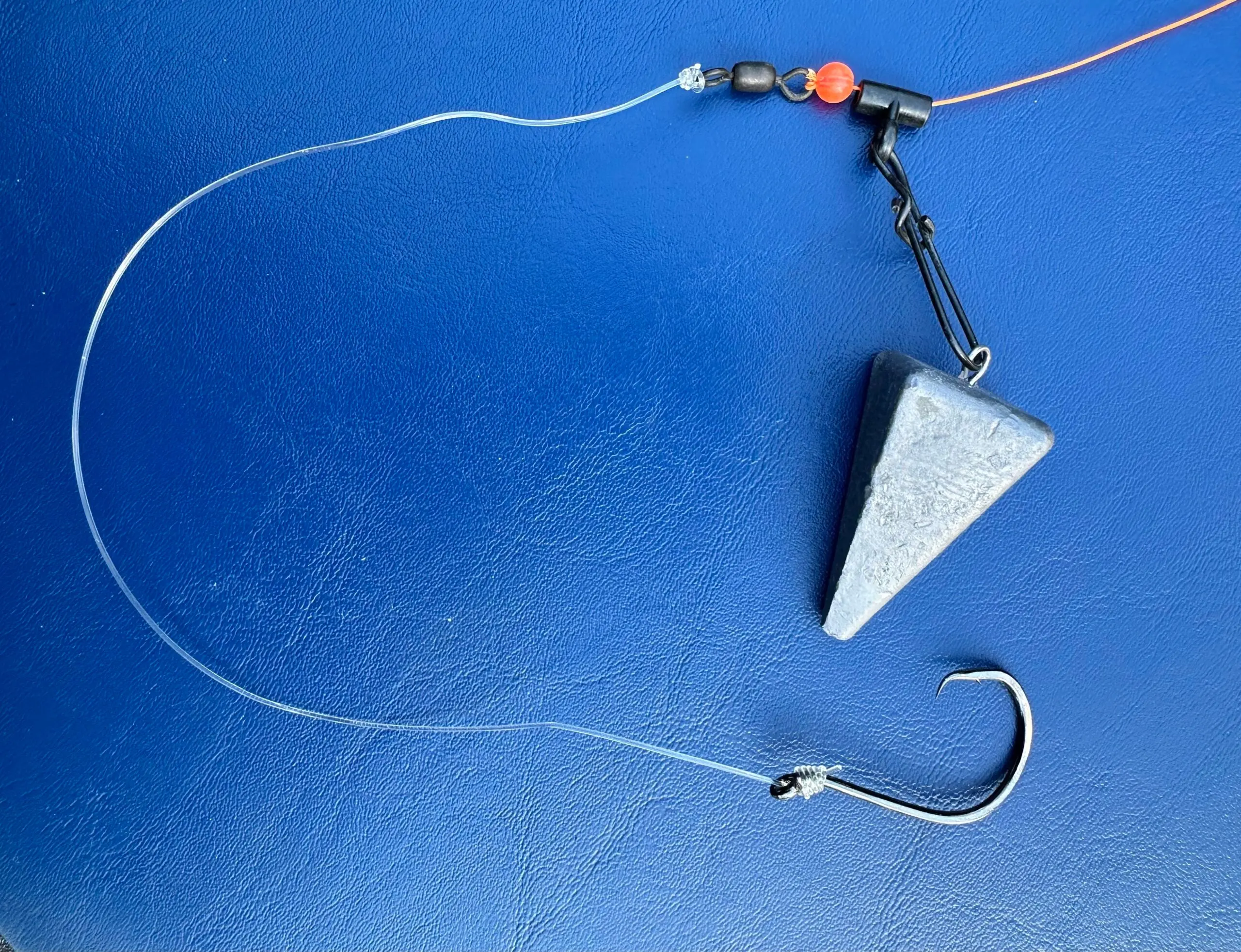 A fishfinder rig for surf fishing featuring a pyramid sinker, fishing hook, and fishing line on a blue surface