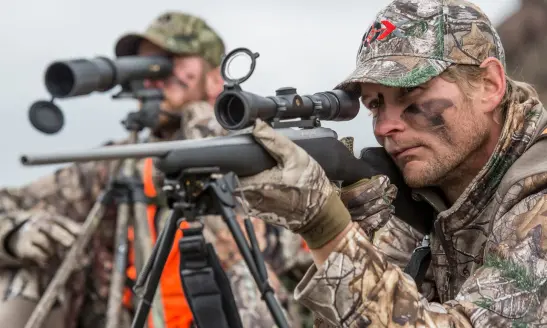 Rifle hunter in Southwest Montana aims at a deer with his partner as spotter.