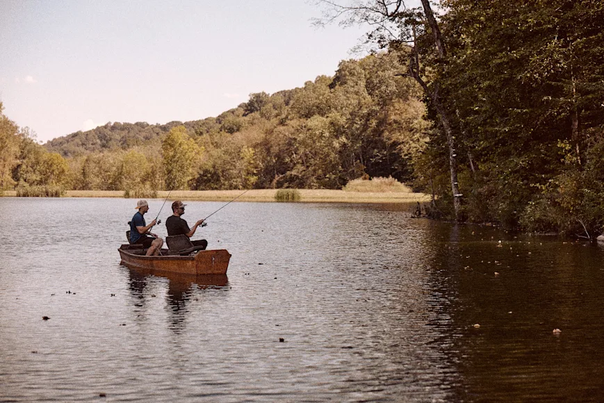 Two fishermen bass fish from a canoe on a pond