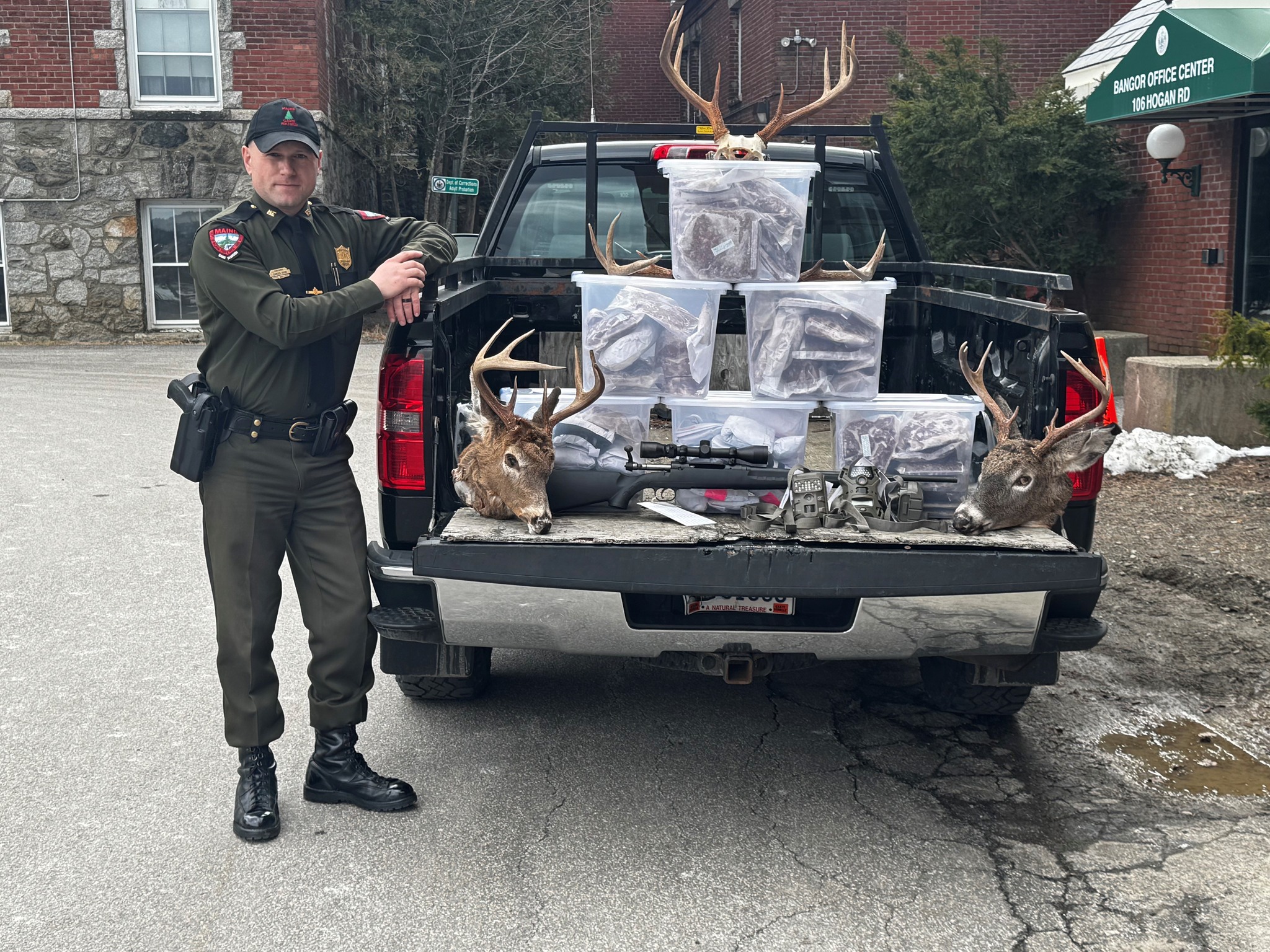 A Maine game warden poses with confiscated deer heads and rifles. 