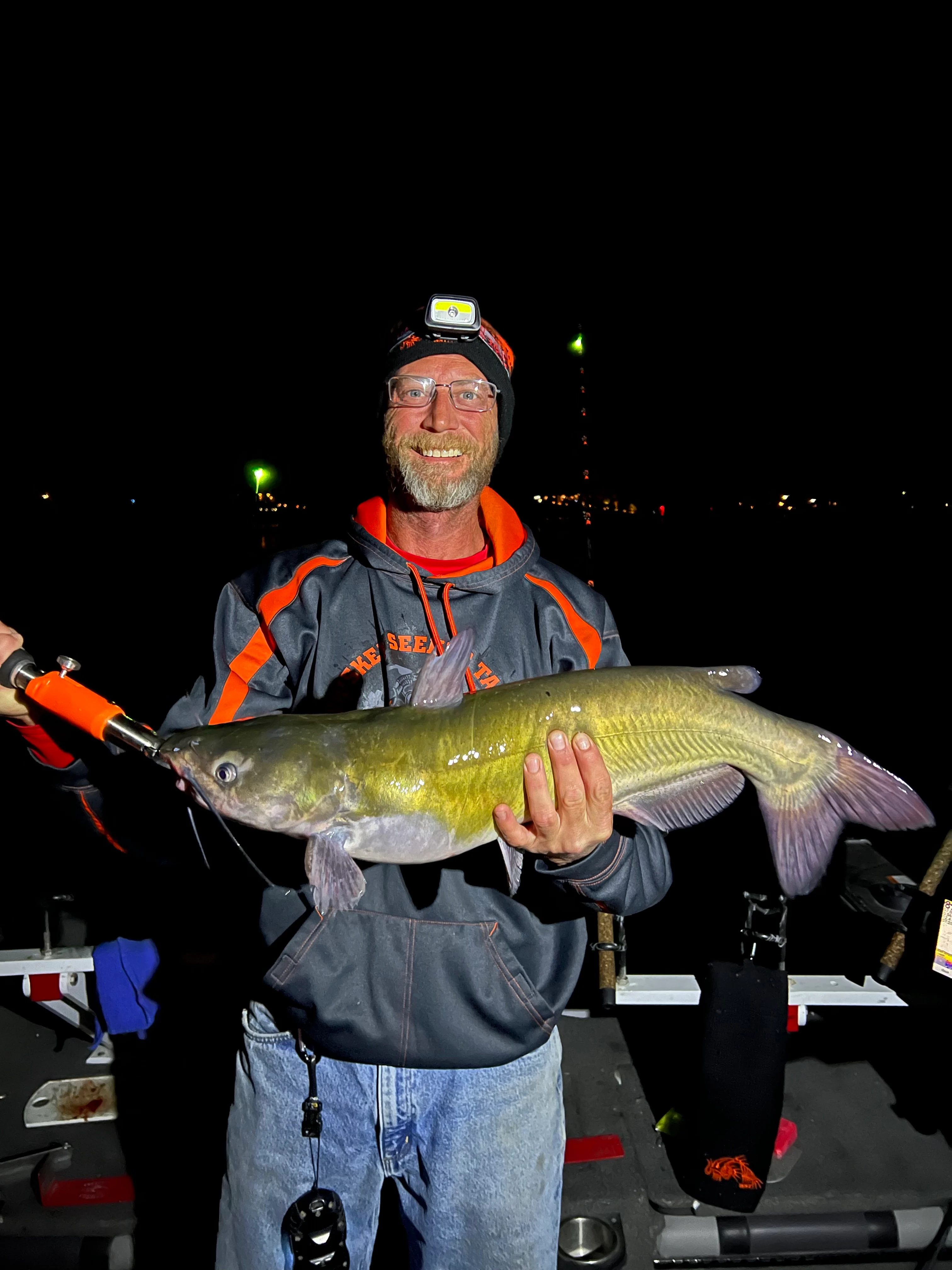 Angler holding up catfish on boat at night.